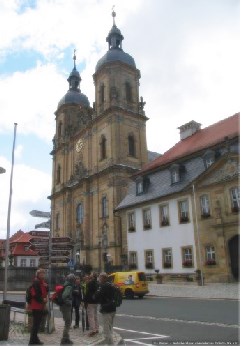 Männer und Frauen mit Rucksäcken stehen an der Straße vor einer Kirche